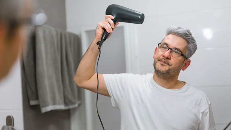 Middle Aged Man Drying Hair In Bathroom With Hairdryer