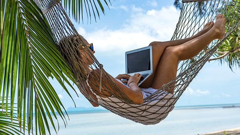 Young woman with a laptop in a hammock on the beach
