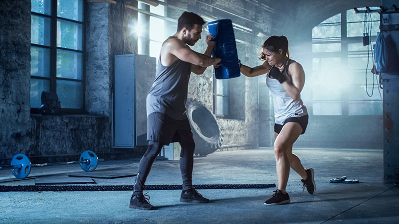 Athletic Woman Hits Punching Bag That Her Partner/ Trainer Holds