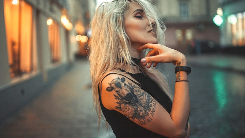 Young Woman Portrait With Tattoo On Shoulder Standing On City St