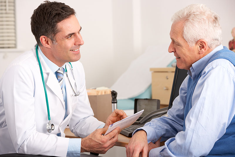 American Doctor Talking To Senior Man In Surgery