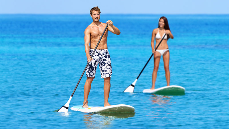 Couple Doing Stand Up Paddleboarding On Ocean