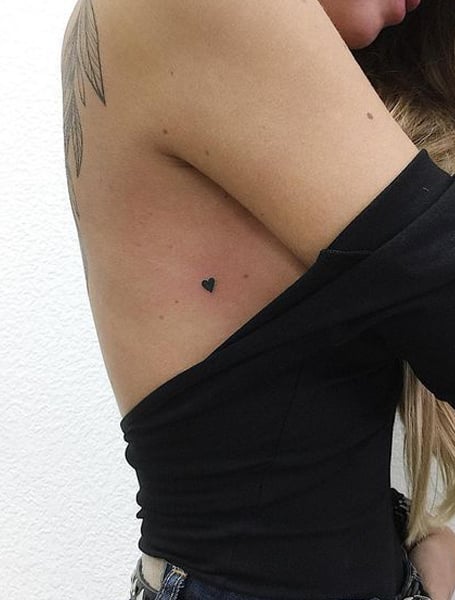 Tiny black heart tattoo on the arm