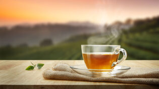 Warm Cup Of Tea And Tea Leaf On Wooden Table With The Tea Planta