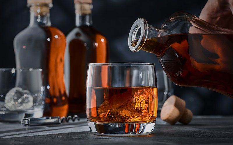Whiskey On The Rocks On The Table, A Bottle With A Drop Of Whiskey On The Neck Above The Glass.