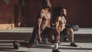Two Multiracial Male Athletes Making Lunges With Weight In Indoor Workout