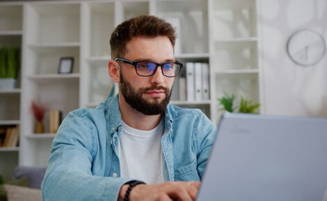 Handsome Caucasian Man Working On Laptop Computer While Sitting Behind Desk In Living Room. Freelancer Male Professional Writing An Important Email From Working From Home.